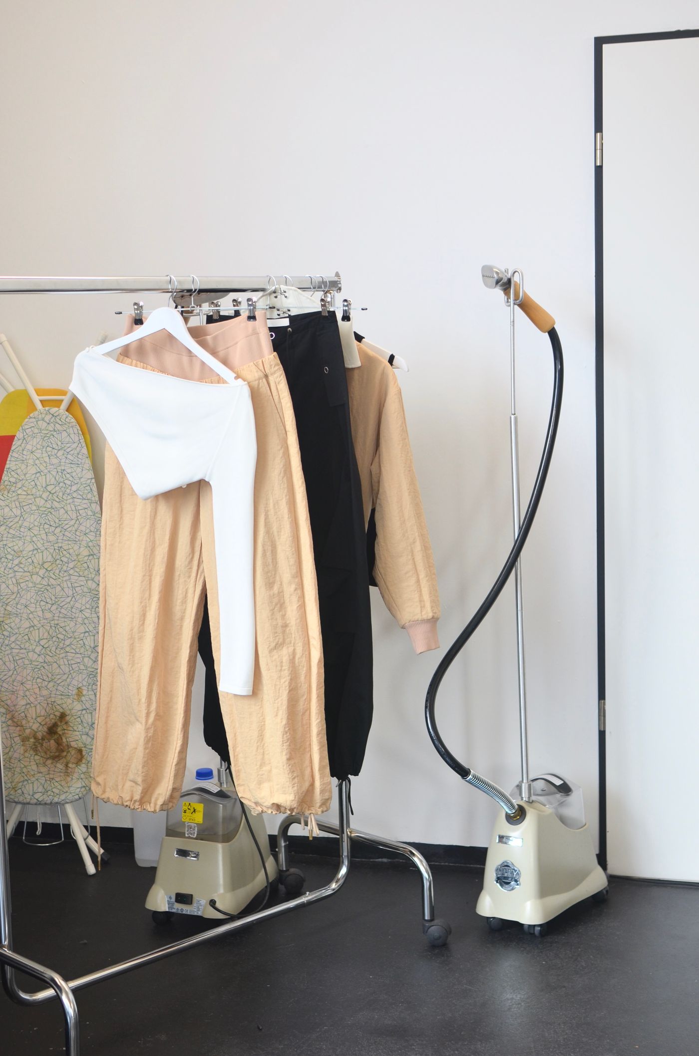 Standing garment steamer beside clothing rack